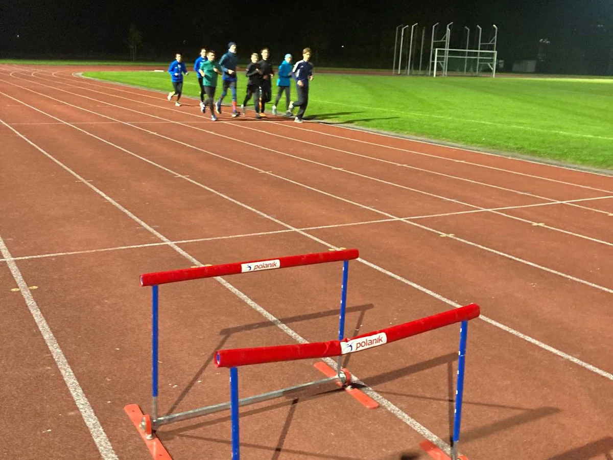 Trainingsgruppe beim Lauftraining auf der Bahn, Hürden im Vordergrund